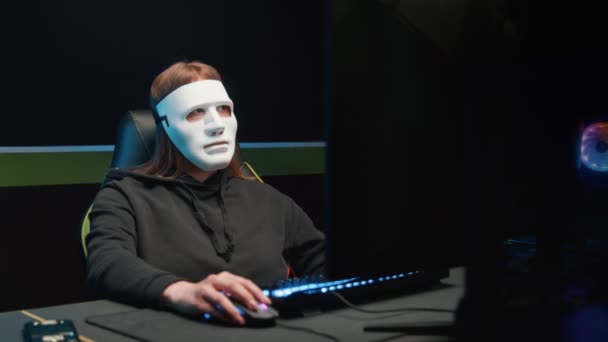 Хакерша за компьютером снимает маску с лица и смотрит в камеру. — стоковое видео