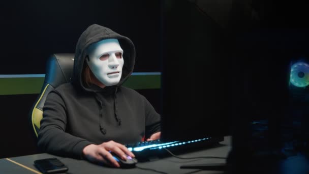 Хакерка за комп'ютером знімає маску з обличчя і дивиться на камеру — стокове відео