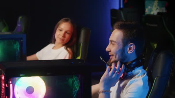 Вид збоку на хлопця і дівчину, що сидить у комп'ютерному клубі, і хлопця показує дівчині щось цікаве на комп'ютері і сміється — стокове відео