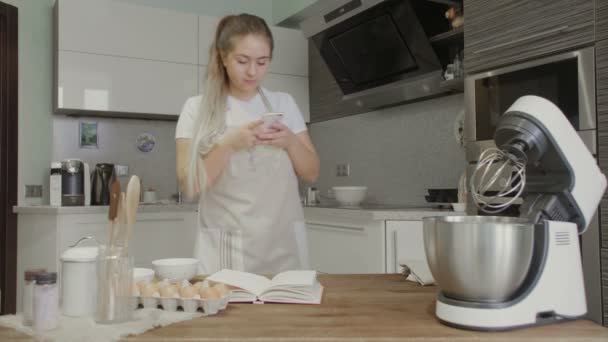 Een meisje in de keuken is op zoek naar recepten op het internet in haar telefoon — Stockvideo