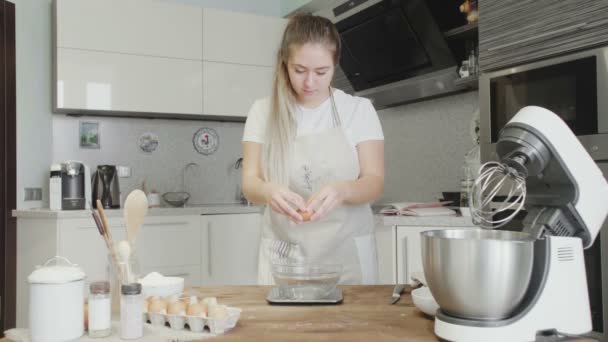 Menina bonita na cozinha quebra um ovo em uma tigela de vidro — Vídeo de Stock