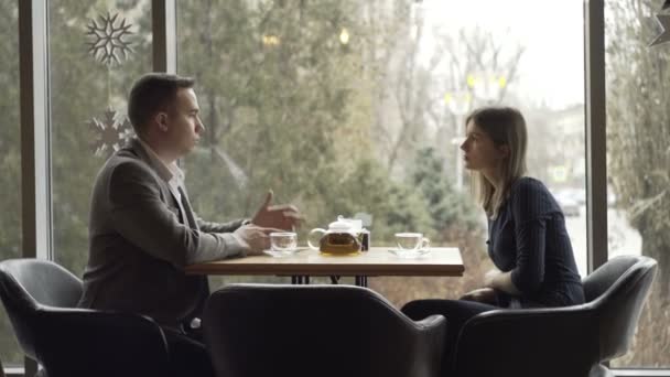 Мужчина и женщина сидят напротив друг друга в кафе или ресторане у окна и общаются. Свидание в кафе или ресторане. Романтическая атмосфера — стоковое видео