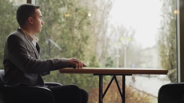Ein Mann sitzt an einem Restauranttisch mit einem Telefon in der Hand — Stockvideo