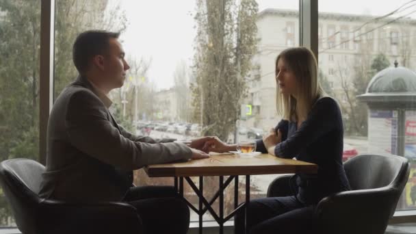 Мужчина и женщина сидят напротив друг друга в кафе или ресторане у окна и общаются. Свидание в кафе или ресторане. Романтическая атмосфера — стоковое видео