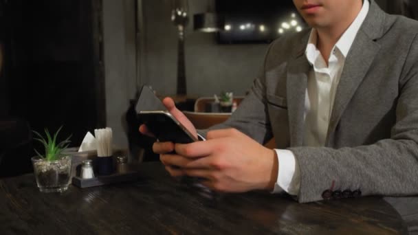 Un homme est assis à une table dans un café, naviguant sur les pages Web sur Internet, une femme se lève par derrière et couvre ses yeux avec ses mains et s'assoit à sa table — Video