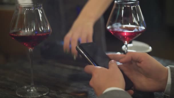 En man på dejt med en kvinna betalar en räkning på ett café eller restaurang med hjälp av NFC närbild — Stockvideo