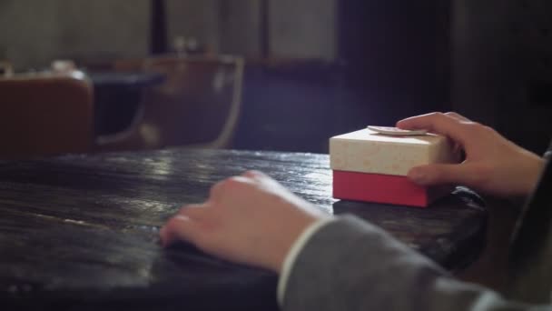 Un hombre toma una caja de regalo de debajo de la mesa y la pone sobre la mesa en un café o restaurante de cerca — Vídeos de Stock