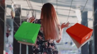 Elbiseli, şık ve genç bir Asyalı müşterinin yakın çekimi ve ellerinde alışveriş torbalarıyla kendi etrafında dönüyor.