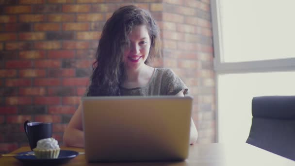 Una giovane donna dai capelli ricci a una scrivania è seduta a un computer e siti web di navigazione — Video Stock