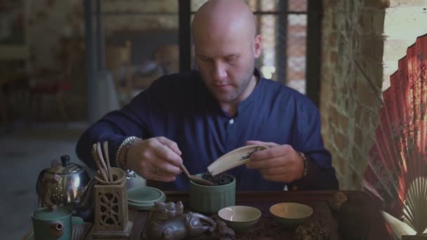 Een jongeman in een theewinkel zet theeblaadjes in een houten lepel met een houten spatel — Stockvideo