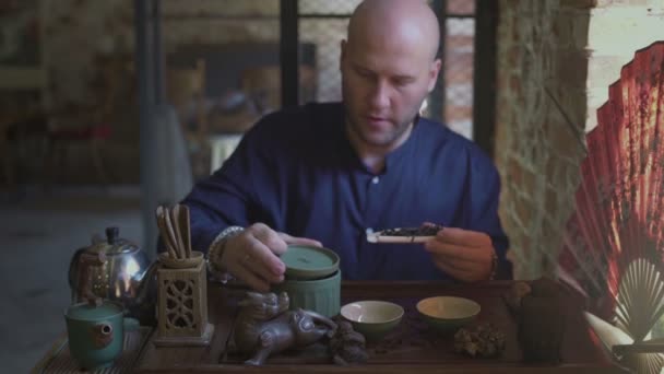 Молодой человек в чайном магазине кладет чайные листья в деревянную ложку с деревянной лопаткой — стоковое видео