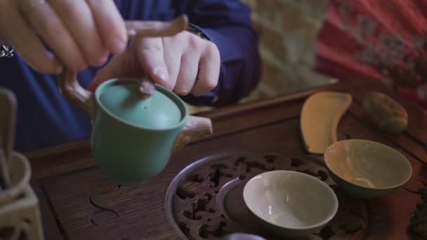 Мужчина наливает чай в чайные чашки на деревянный поднос в чайной комнате — стоковое видео