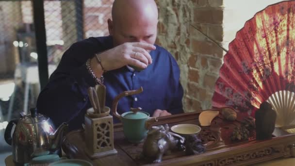 Een man drinkt groene thee uit een theeservies in een theekamer — Stockvideo