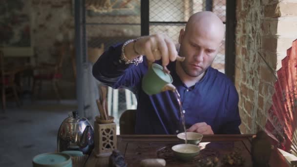 Een man giet thee in theekopjes op een houten dienblad in een theekamer — Stockvideo