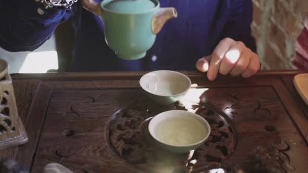 Un bărbat toarnă ceai în cești de ceai pe o tavă de lemn într-o cameră de ceai — Videoclip de stoc