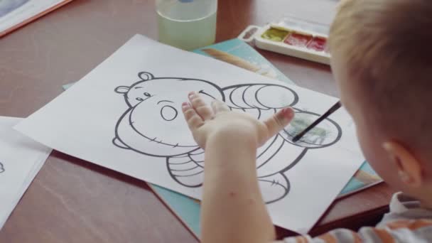 Bakifrån en liten pojke ritar en målarbok med en flodhäst med en pensel — Stockvideo