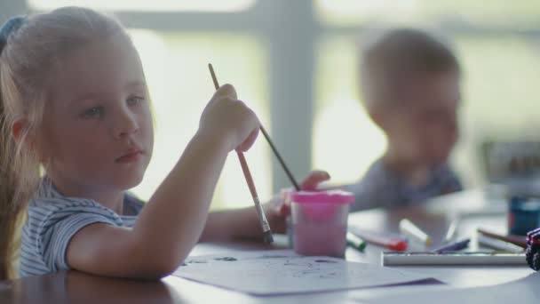 Děti sedí u stolu a kreslí na papír s různými barvami a štětci — Stock video