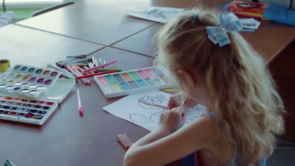 Una bambina è seduta a un tavolo e disegna su carta con colori e pennelli diversi — Video Stock