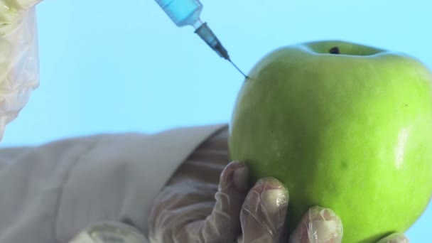 Zbliżenie człowieka w płaszczu medycznym i rękawiczki wstrzykujące strzykawkę do jabłka z płynem na niebieskim tle — Wideo stockowe