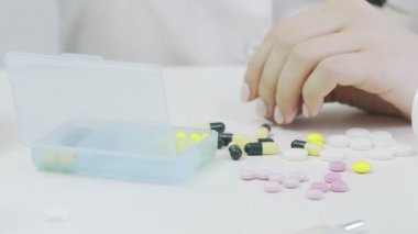 Farklı tabletlerle bir ilaç kutusuna yakın çekim. Bir insan eli ilaç kutusuna koyar.
