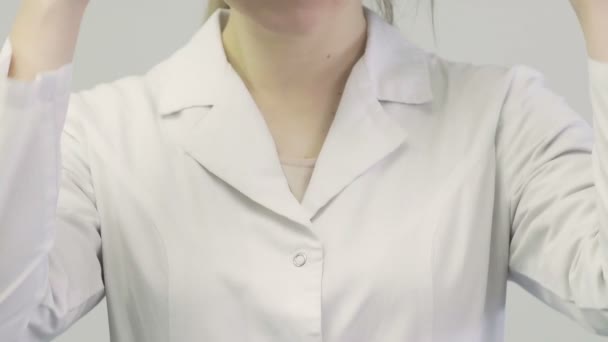 Primer plano de un médico una mujer con una bata médica se pone un estetoscopio en el cuello — Vídeos de Stock