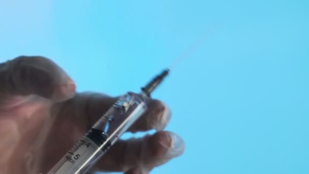 使い捨て注射器からの針の閉鎖。小さな注射器が青い背景に穴から液体を押し出す — ストック動画