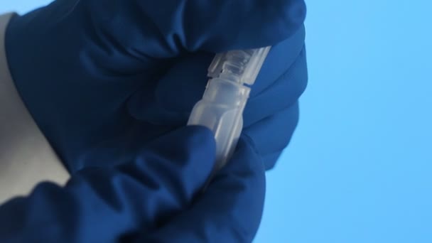 Close-up van een hand in latex handschoenen die een plastic ampul van het vaccin openen op een blauwe achtergrond — Stockvideo