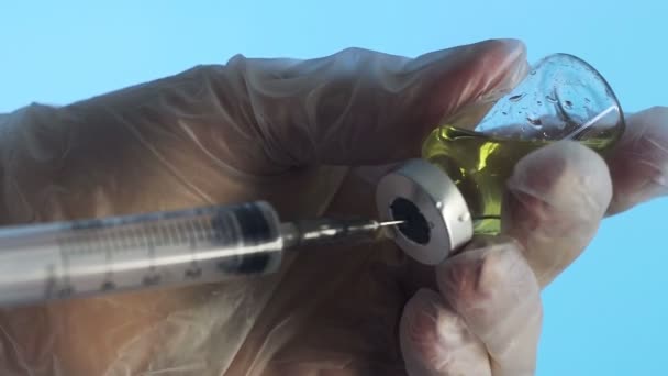 Primer plano de las manos de un médico que prepara una vacuna inyectable sobre un fondo azul — Vídeo de stock