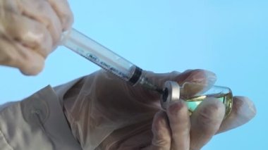 Doktorun elleri mavi arka planda aşı için aşı hazırlıyor.