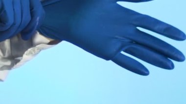 Kadınların elleri ellerine ikinci bir tıbbi eldiven takar. Mavi arkaplanda yakın plan