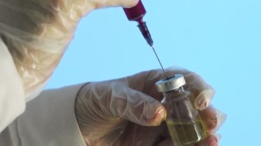 Doktorların elleri temiz çözeltili bir şırınga tutarken ve ampulün içine kırmızı bir madde dökerken. Bir tıp laboratuarında aşı geliştirme süreci, deneysel araştırmalar.