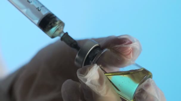 Close-up de um médico mãos preparando uma vacina para injeção em um fundo azul — Vídeo de Stock