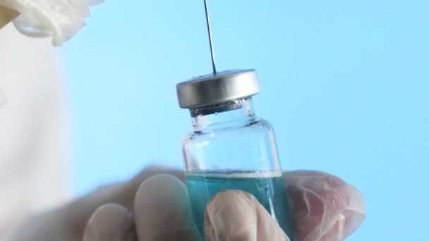 Gros plan des mains d'un médecin préparant un vaccin injectable sur fond bleu — Video