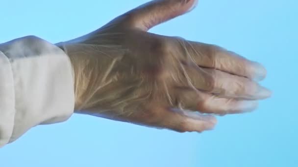 Vrouwenhanden doen een tweede transparante medische handschoen om hun hand. Close-up op een blauwe achtergrond — Stockvideo