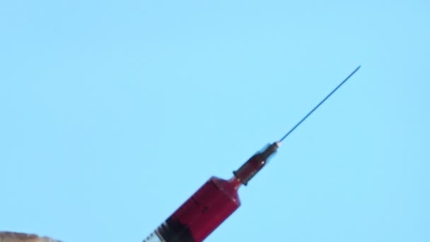 Närbild av en nål från en engångsspruta. En liten spruta trycker ut en röd vätska ur hålet på en blå bakgrund — Stockvideo