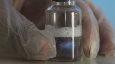 Doktorların elleri temiz çözeltili bir şırınga tutarken ve ampulün içine kırmızı bir madde dökerken. Bir tıp laboratuarında aşı geliştirme süreci, deneysel araştırmalar.