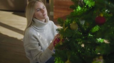 Süveter giyen genç ve güzel bir sarışın Noel ağacının yanında oturuyor ve bir Noel balosu düzenliyor. Evin penceresinin yanında altında hediyeler olan bir Noel ağacı..