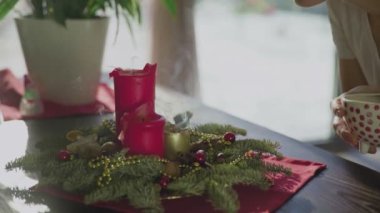 Tanınmayan bir kız, iki kırmızı mum ve bir altın mumla her daim yeşil bir çelenk üflüyor. Noel arifesinde Hıristiyanların gelenek ve adetleri. Bayramın sembolü..