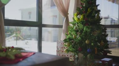 İki kırmızı mum ve bir altın mumu olan ebedi yeşil bir çelenk. Arka planda süslü bir Noel ağacı var. Noel arifesinde Hıristiyanların gelenek ve adetleri.