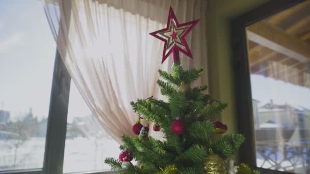 Un sapin de Noël décoré à côté de la fenêtre de la maison. Nouvel An. — Video