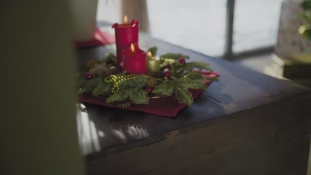 Une couronne à feuilles persistantes avec deux bougies rouges et une bougie dorée. Traditions et coutumes de Noël des chrétiens à la veille de la fête. — Video