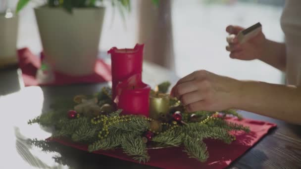 An unrecognizable girl lights an evergreen wreath with two red candles and one golden candle. Christmas traditions and customs of Christians on the eve of the holiday. A symbol of the holiday. — Stock Video