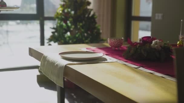 Una chica irreconocible pone un plato con una bola de Navidad sobre la mesa. Preparándose para la Navidad, sirviendo una mesa festiva en la casa. Las tradiciones navideñas. — Vídeos de Stock