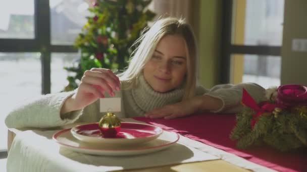 한 젊고 아름다운 여성 이 새로운 해의 공을 보면서 손으로 탁자에 기대고 있습니다. 크리스마스 준비중이야. 불쾌 한 기분. — 비디오