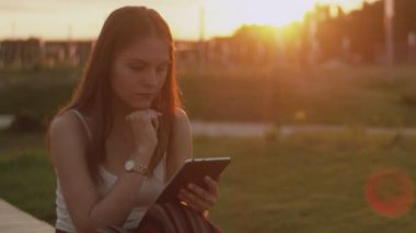 Gün batımında parkta bir kız e-kitap okuyor.