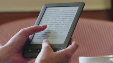 Bir kafede kadınların elleri bir e-kitap tutuyor.