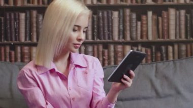 Kız kütüphanede oturuyor ve e-kitap okuyor.