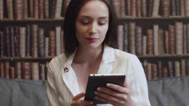 La ragazza è seduta in biblioteca e legge un e-book — Video Stock