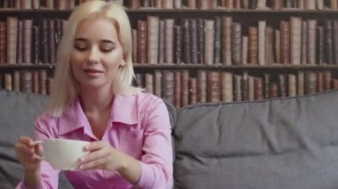 Bir kız kütüphanede bir fincan kahve içip e-kitap okuyor.