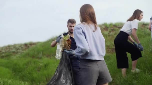 Os amigos recolhem lixo num saco de lixo. Poluição plástica e conceito de problema ambiental. Limpeza voluntária da natureza do plástico. — Vídeo de Stock